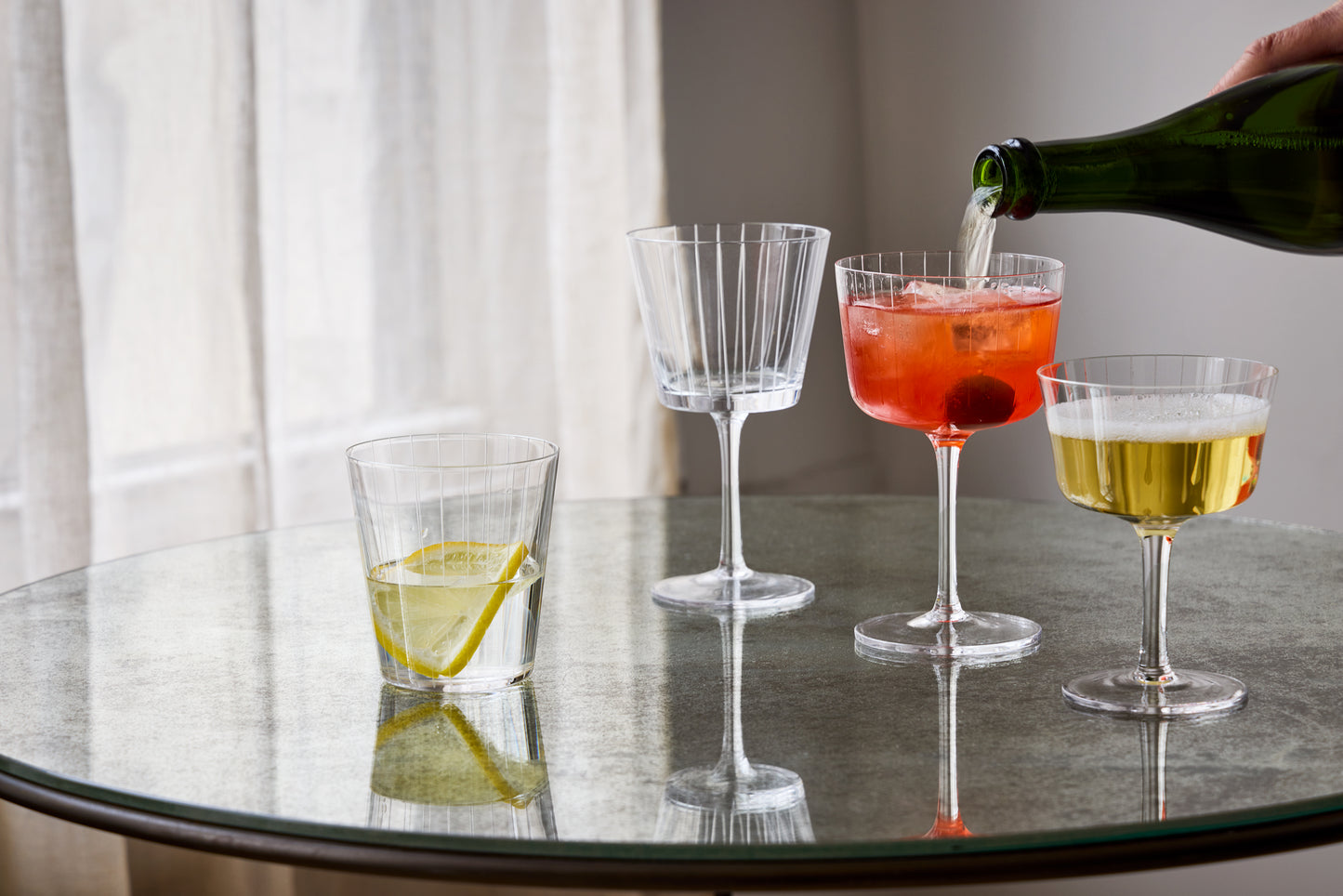 Cocktails being poured into glasses on a reflective surface with a neutral background