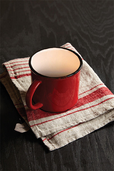 Rustic red distressed stoneware mug on linen striped tea towel on wooden black table